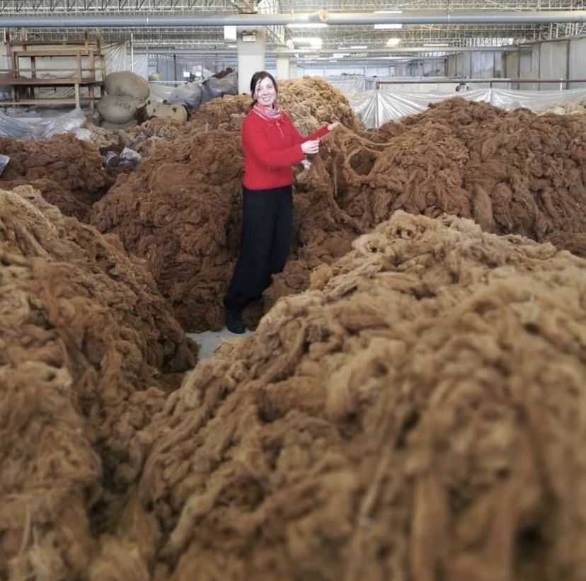 Mia i en hög av alpacka råvara på fabriken i Peru
